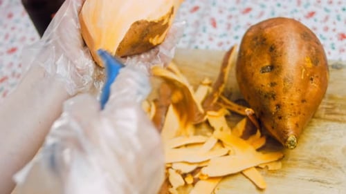 Person Peeling a Sweet Potato on Cutting Board