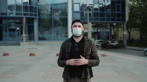 Mann mit medizinischer Maske spricht selbstbewusst mit Gesten in die Kamera im Stadtgebiet