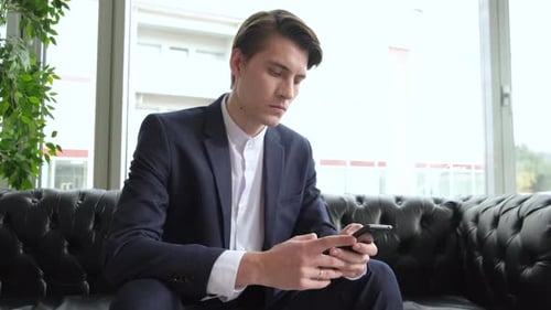 Male millennial professional holding modern smartphone texting message in office