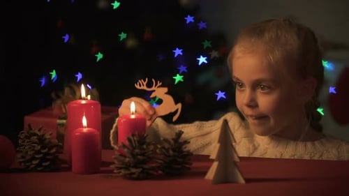 Girl Plays with Ornaments by Candles at Christmas