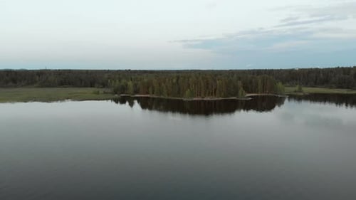 Aerial decending tilt view of a island coast, above a tranquil and serene lake, at a sunny autumn du