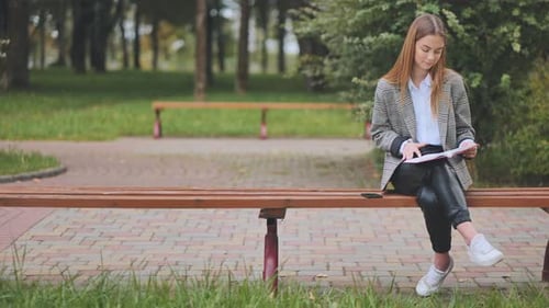 A Girl Sits on a Park Bench and Reads a Book