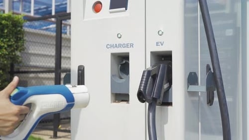 Hand pulling in cable from EV car charger or electric vehicle station. Cable connected