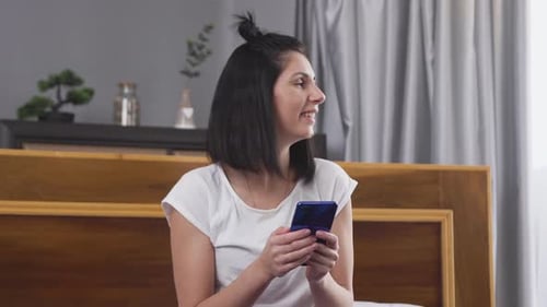 Woman Using Smartphone on Bed in Bedroom