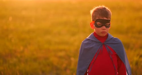 A Child in the Costume of a Superhero in a Red Cloak Runs Across the Green Lawn Against the Backdrop