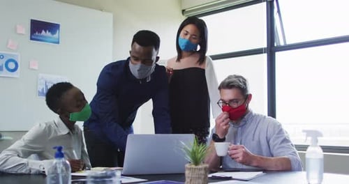 Office colleagues wearing face masks using laptop together in meeting room at modern office