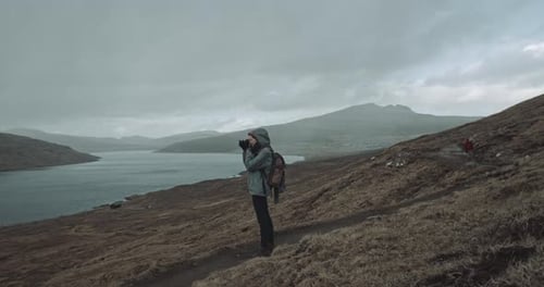 Two people walk together in the mountains, one stops and takes photo