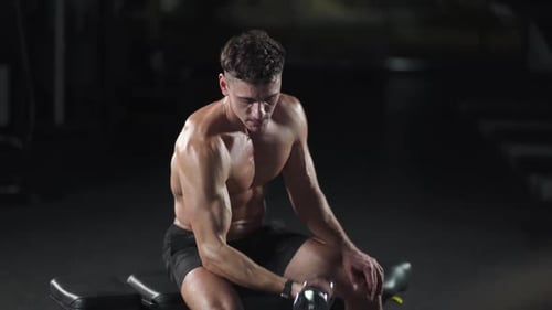 Athletic Man trainiert im Fitnessstudio, hebt Hanteln und führt Übungen für Arme und Bizeps durch.
