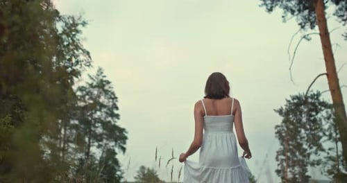 Girl in a White Dress Walks in a Meadow, High Beautiful Grass. Girl Touches and Straightens the