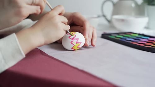 Child with mom paints an Easter egg