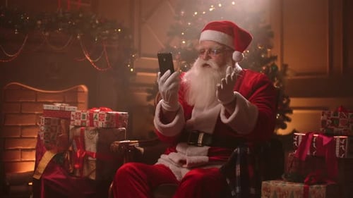 Santa Claus Is Communicating By Video Call at Smartphone, Sitting in His Residence at Christmas