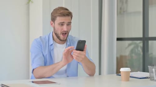 Young Creative Man Reacting to Loss on Smartphone in Office