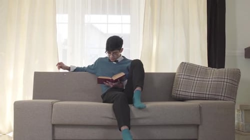 Portrait of Focused Caucasian Young Man Sitting on Sofa and Reading. Handsome University Student
