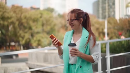 Beautiful business woman in glasses smiles and using mobile phone texting street