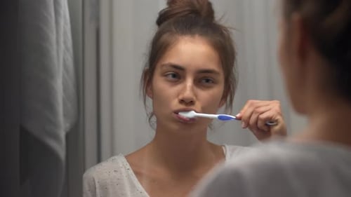 Woman Brushing Teeth in Bathroom Mirror