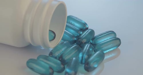 Blue Medication Capsules Falling from Bottle