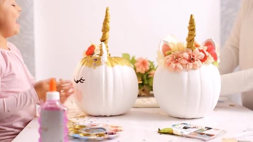 Little girl and her mother painting face of a unicorns on her craft pumpkin for Halloween.