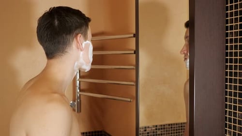Homem bonito se barbeia na frente de um espelho