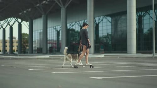 Young Beautiful Woman Riding on Skateboard or Longboard on the Street with Her Husky Dog