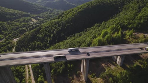 Aerial View of White Cargo Semi Truck Driving on Two Way Motorway Viaduct Over Green Hills