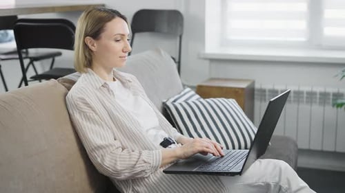 Woman Relaxing on Couch Typing on Laptop