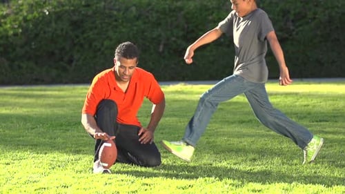 Adult and Child Kicking Football on Grassy Field