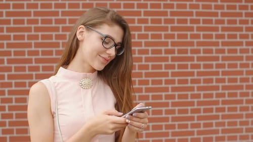 Woman Using Smartphone in front of Brick Wall