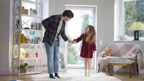 Handsome Young Caucasian Man Taking Hand of Playful Pretty Girl and Dancing with Child