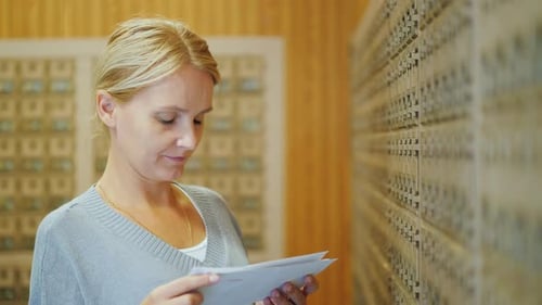 Attractive Woman Looks Through Letters in the Post Office on the Background of Mailboxes