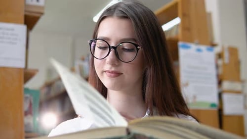 A Thoughtful Young Student Reads a Book Standing in the Library