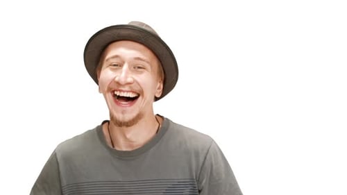 Junger gutaussehender Mann mit Hut lacht und zeigt mit dem Finger auf die Kamera auf weißem Hintergrund