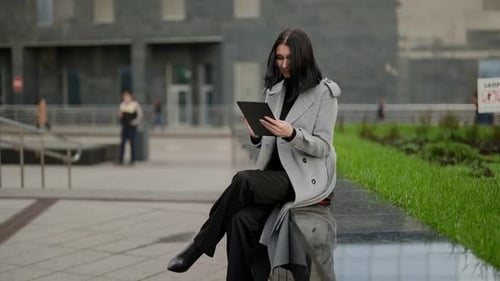 Woman Using Tablet Sitting Outdoors in City
