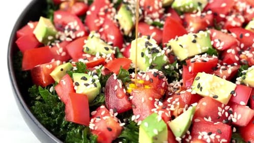 Salade de chou frisé aux tomates et à l'avocat dans une assiette noire.