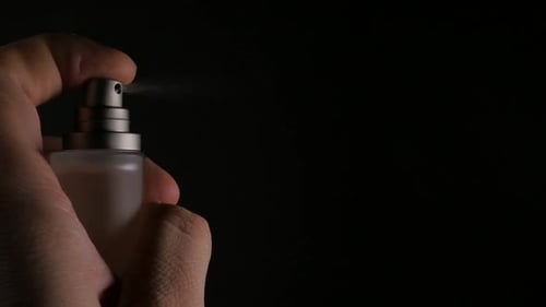 Hand Sprays Small Bottle on Black Background