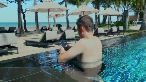 Young Man Using Smartphone in Swimming Pool at Luxury Tropical Hotel Resort