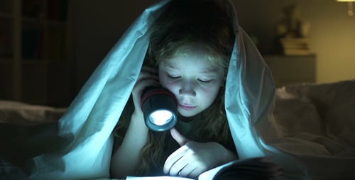 Girl Reading with Flashlight Under Blanket at Night