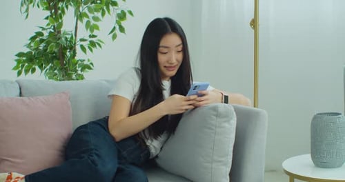 Young Woman Relaxing on Couch Using Mobile Phone