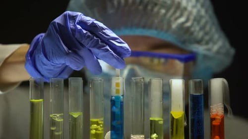 Scientifique mesurant le niveau d'acidité dans un tube avec un liquide bleu dans un laboratoire sombre