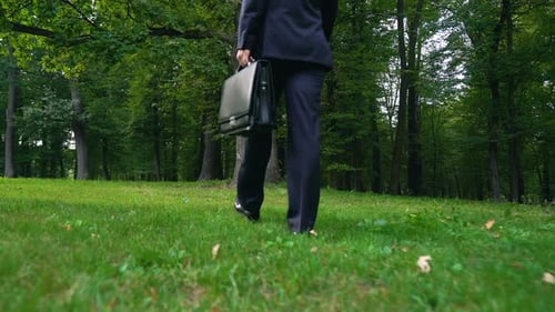 Mann verlässt Aktentasche auf Gras und spaziert im grünen Wald, Flucht vor Stress