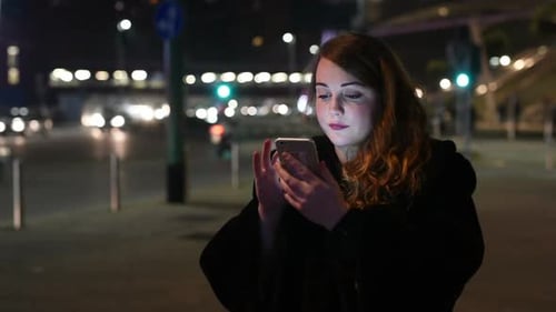Young Woman Using Phone on City Street at Night