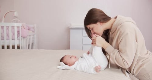 Loving Mother Kisses Infant's Foot on Bed