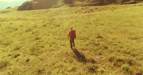 Flight Over Backpack Hiking Tourist Walking Across Green Mountain Field. Huge Rural Valley at Summer