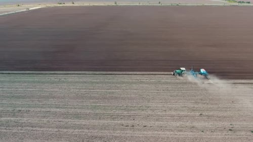 Aerial Shot of a Wide Agriculture Field with a Tractor Ploughing It in Autumn