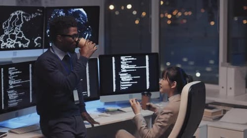 Colleagues Chatting in Front of Computer Monitors at Night
