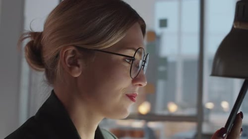 Pretty Woman Smiling and Texting on Smartphone at Office Desk