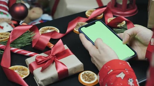 Female fingers are watching christmas presents online on cell phone with green screen