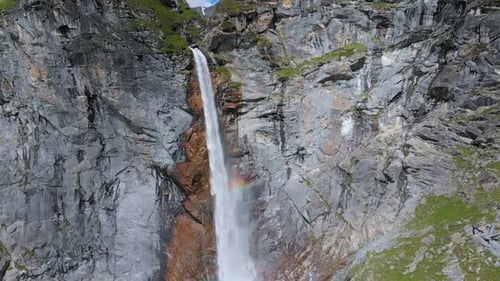 Aerial slow motion: drone flying over scenic high waterfall, mountain stream falling from cliff
