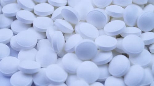 A Large Number of White Vitamins Lie Nearby and Rotate on the Table Close-up