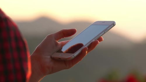 Hand Holding Smartphone at Sunrise or Sunset