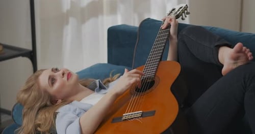 Woman Plays Acoustic Guitar Lying on Sofa